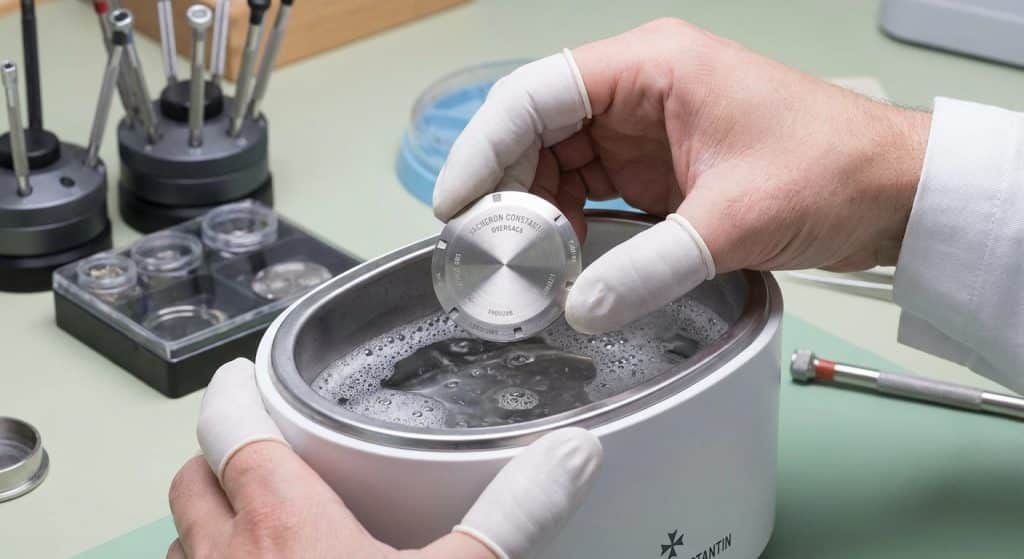 A professional watchmaker performs an ultrasonic cleaning of a 904L steel Overseas case-back to remove galvanic build-up before re-sealing.