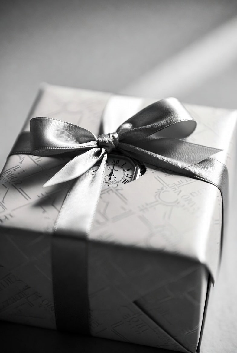 A beautifully wrapped gift box with a Cartier-style watch peeking out, hinting at luxury without revealing authenticity.