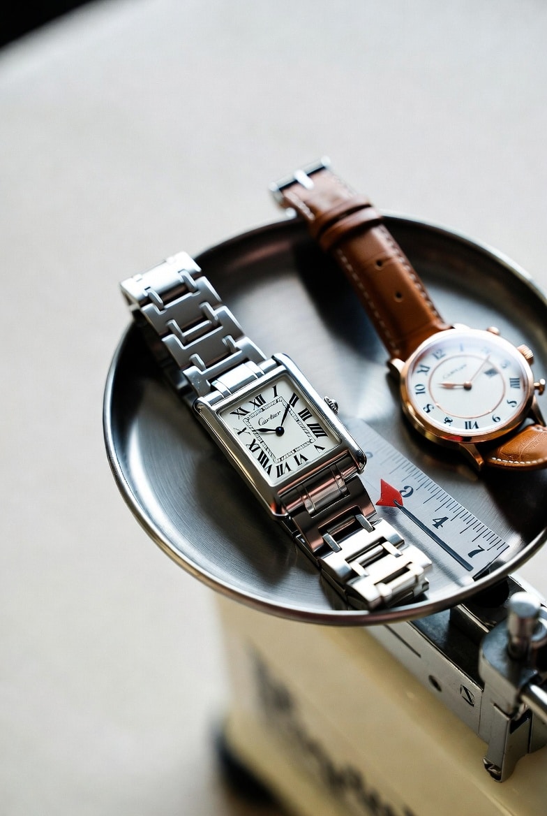 A close-up of a Cartier watch on a scale, with another watch nearby, illustrating the concept of weight comparison.
